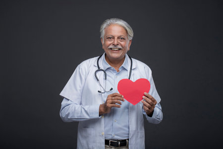 Portrait of a senior doctor holding a red heart on black backgroundの写真素材