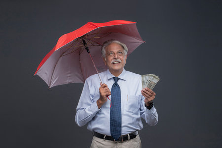 business man holding umbrella and money in hand, on grey backgroundの写真素材