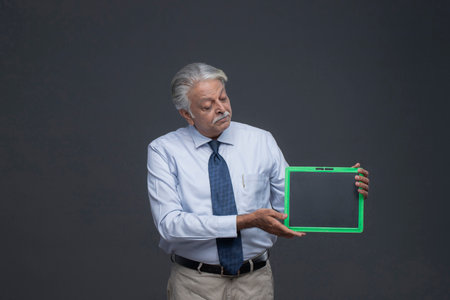 Senior businessman holding a green tablet computer with blank screen, grey backgroundの写真素材