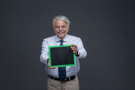 Portrait of senior Asian teacher holding green chalkboard on grey backgroundの写真素材