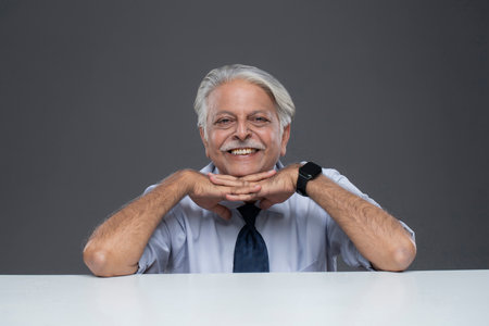 Portrait of happy senior businessman sitting at table isolated on grey backgroundの写真素材