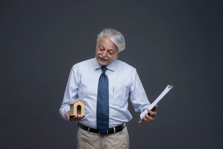 asian senior business man holding a model house and documents on grey backgroundの写真素材