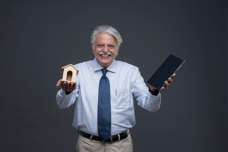 asian senior man holding a house model and a book on grey backgroundの写真素材