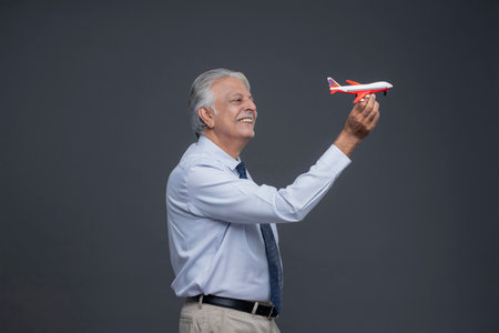 Happy senior man holding toy airplane and smiling at camera on grey backgroundの写真素材