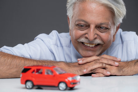 Smiling senior man sitting at table with toy car on grey backgroundの写真素材
