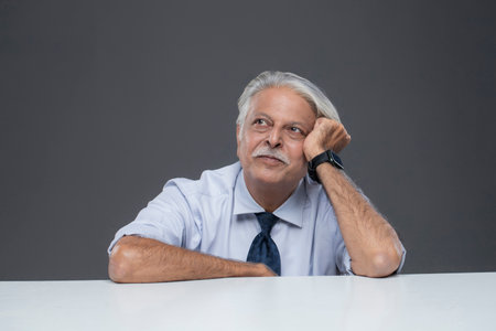 Portrait of a senior businessman sitting at his desk against grey backgroundの写真素材