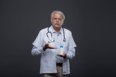 senior doctor with stethoscope holding medicine bottle on black backgroundの写真素材