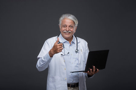 Portrait of senior doctor holding laptop and showing thumbs up. Isolated on black backgroundの写真素材