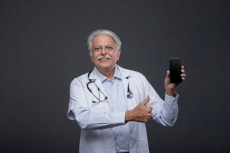 Portrait of senior doctor with stethoscope and mobile phone on grey backgroundの写真素材