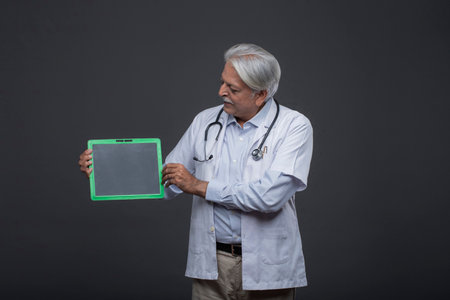 Senior doctor holding a green clipboard and looking at the camera. Gray background.の写真素材