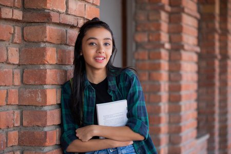 Portrait of a smiling female college student standing by a brick wallの写真素材