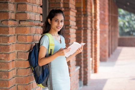 Portrait of a smiling female college student reading a book in campusの写真素材