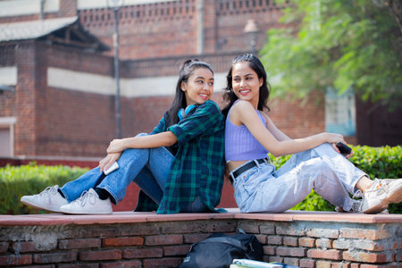 Two young asian women sitting on the wall in the park.の写真素材