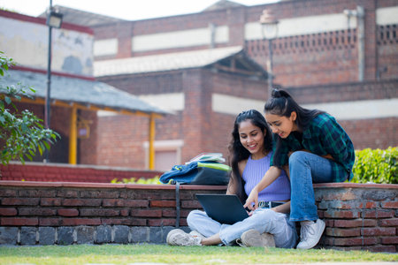 Portrait of two students sitting on bench and using laptop in campusの写真素材
