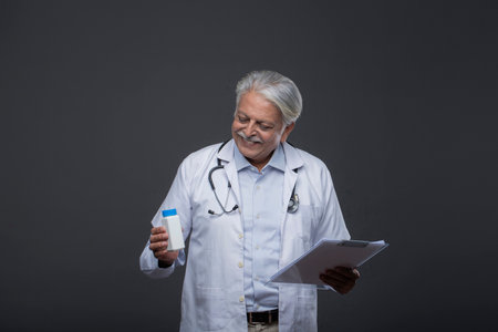 Senior doctor holding a bottle of medicine and looking at tablet on grey backgroundの写真素材
