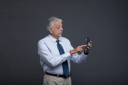 Senior man using mobile phone on grey background. Asian male model with grey hair and blue shirt.の写真素材