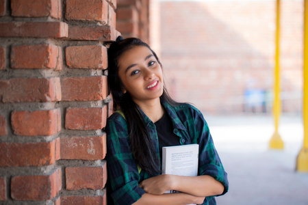 Portrait of smiling college student leaning against brick wall in college campusの写真素材