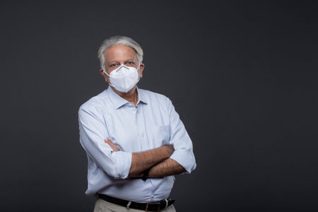 senior businessman in medical mask standing with crossed arms isolated on greyの写真素材