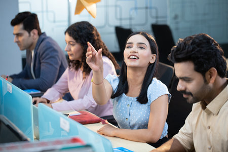 Smiling businesswoman sitting at desk with colleagues in background at officeの写真素材