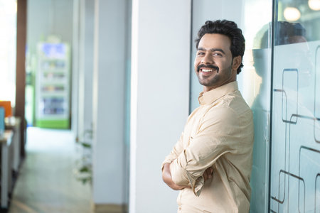 Portrait of smiling young Indian businessman standing with arms crossed in office