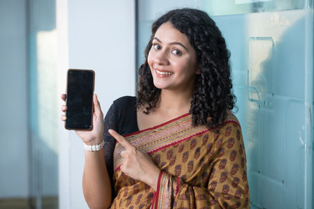 Portrait of smiling young woman showing smartphone with blank screen in corridor