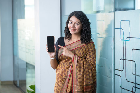 Portrait of smiling woman showing mobile phone in corridor of modern office