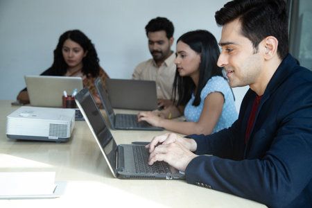 Portrait of smiling businessman using laptop with colleagues in background at office