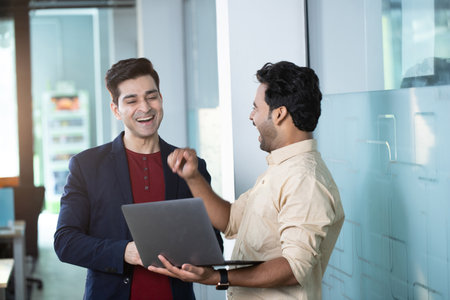 Portrait of two business executives discussing over laptop while standing in officeの写真素材
