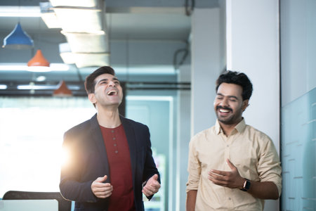 Portrait of two young business people laughing and smiling while standing in officeの写真素材