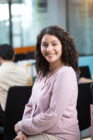 Portrait of smiling businesswoman sitting on chair in office with colleagues in background