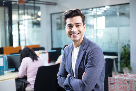 Portrait of smiling businessman standing with arms crossed at desk in office