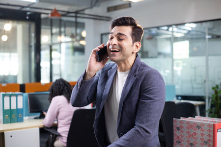 Portrait of smiling businessman talking on mobile phone while colleague working in background at...