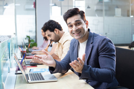 Portrait of smiling businessman using laptop while colleagues discussing in background at office
