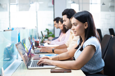 Portrait of businesswoman using laptop in office with colleagues on background