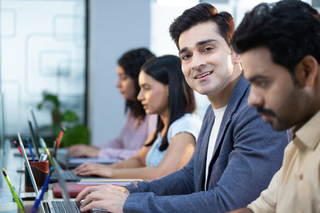 Portrait of confident businessman looking at camera while colleagues working in background