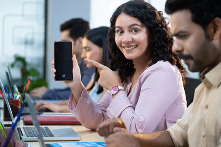 Portrait of smiling businesswoman showing mobile phone to colleagues in officeの写真素材