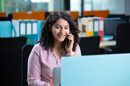 Portrait of smiling businesswoman using mobile phone while sitting at desk in office