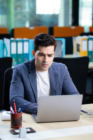 Serious businessman working on laptop at office desk in front of him