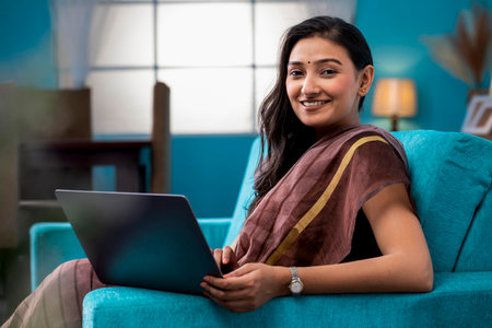 Portrait of a smiling woman using laptop while sitting on sofa at homeの写真素材
