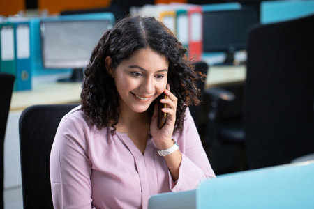 Portrait of smiling businesswoman talking on mobile phone while sitting at desk in officeの写真素材
