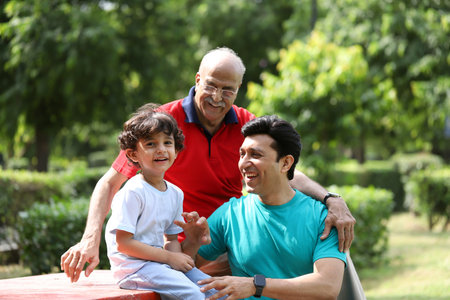 Grandfather, grandfather and grandson sitting on bench in park on summer day