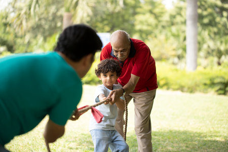 Grandfather Helping Grandson Pulling Tug Of War In Park