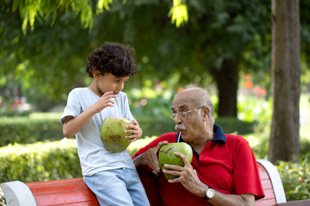Grandfather and grandson drinking coconut juice in the park. Concept of healthy lifestyle.