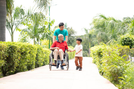 Happy asian elderly man in wheelchair with his grandson in the park