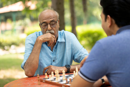 Senior man playing chess with his grandson in the park. Senior people retirement concept.