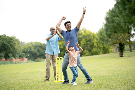Happy Indian family with son and grandson playing cricket in the park.の写真素材