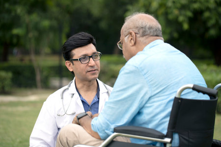Asian male doctor talking with senior patient in wheelchair in the park.の写真素材