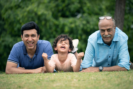 Portrait of three generations of family lying together on green grass in parkの写真素材