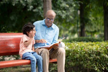 Grandfather and grandson sitting on bench in park and reading book togetherの写真素材