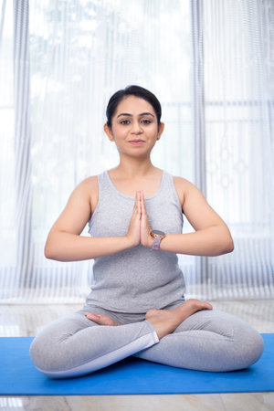 Portrait of young woman meditating in lotus position at home